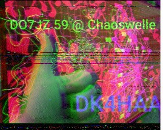 A decoded SSTV image of a hand giving the thumbs up sign with the text "DO7JZ 59 @ Chaoswelle DK4HAA"